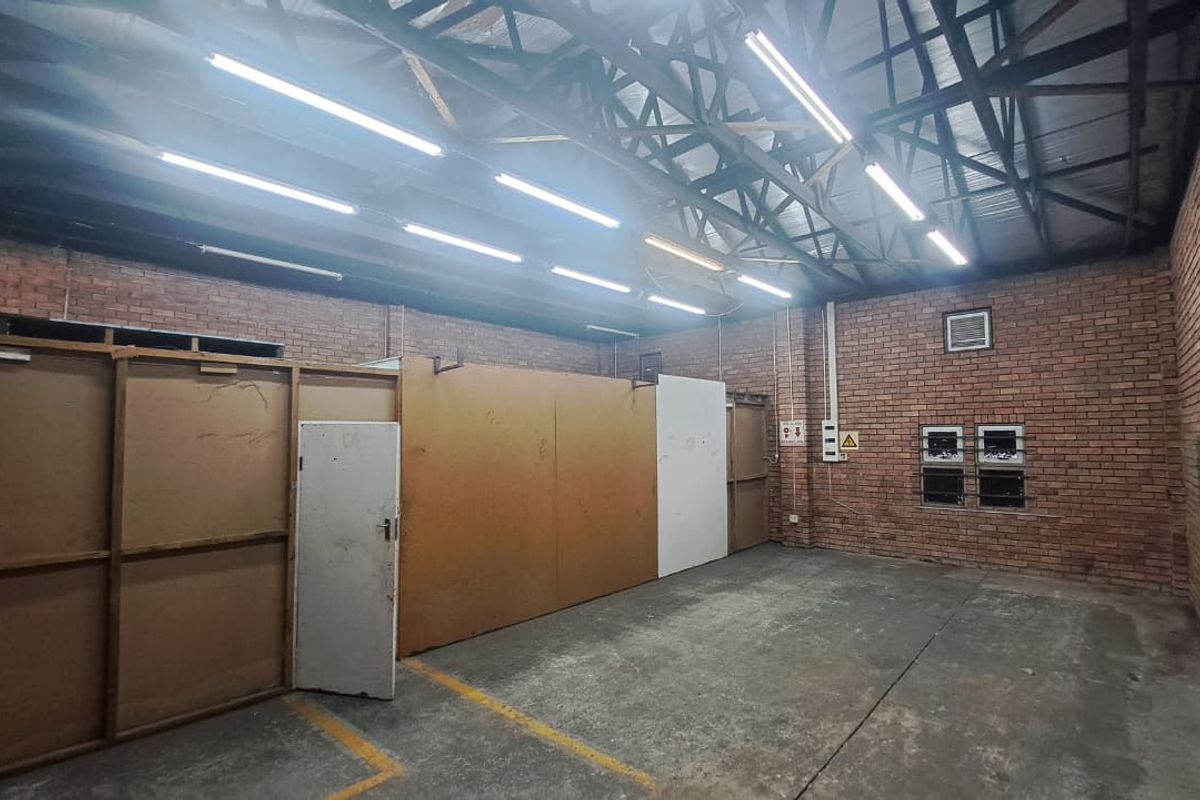 Spacious industrial utility area featuring exposed brick walls, high steel roof trusses, concrete flooring, and functional overhead fluorescent lighting.