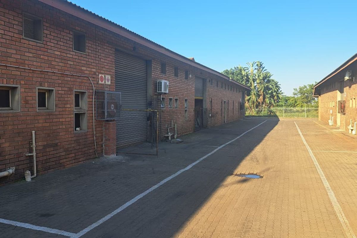 Exterior view of an industrial property featuring face brick facades, multiple roller shutter doors, and a paved driveway area.