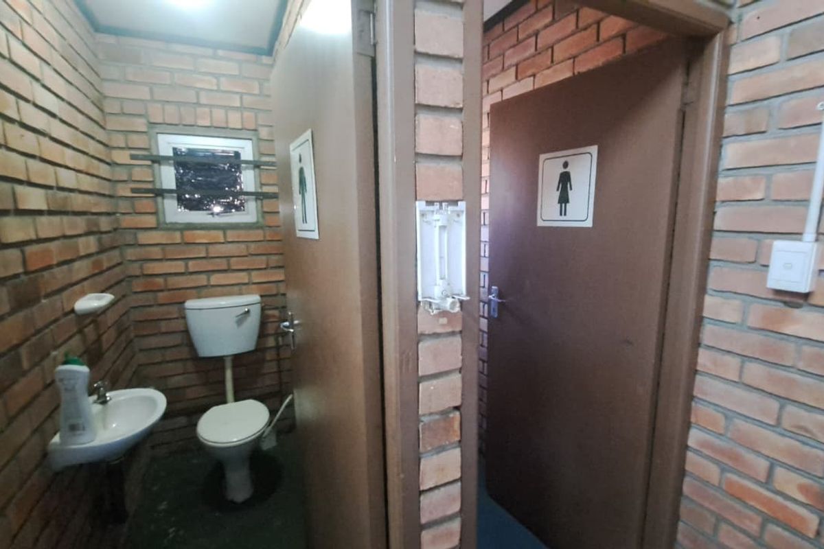 Functional industrial-style bathroom featuring exposed brick walls, a wall-mounted basin, and a separate toilet cubicle.