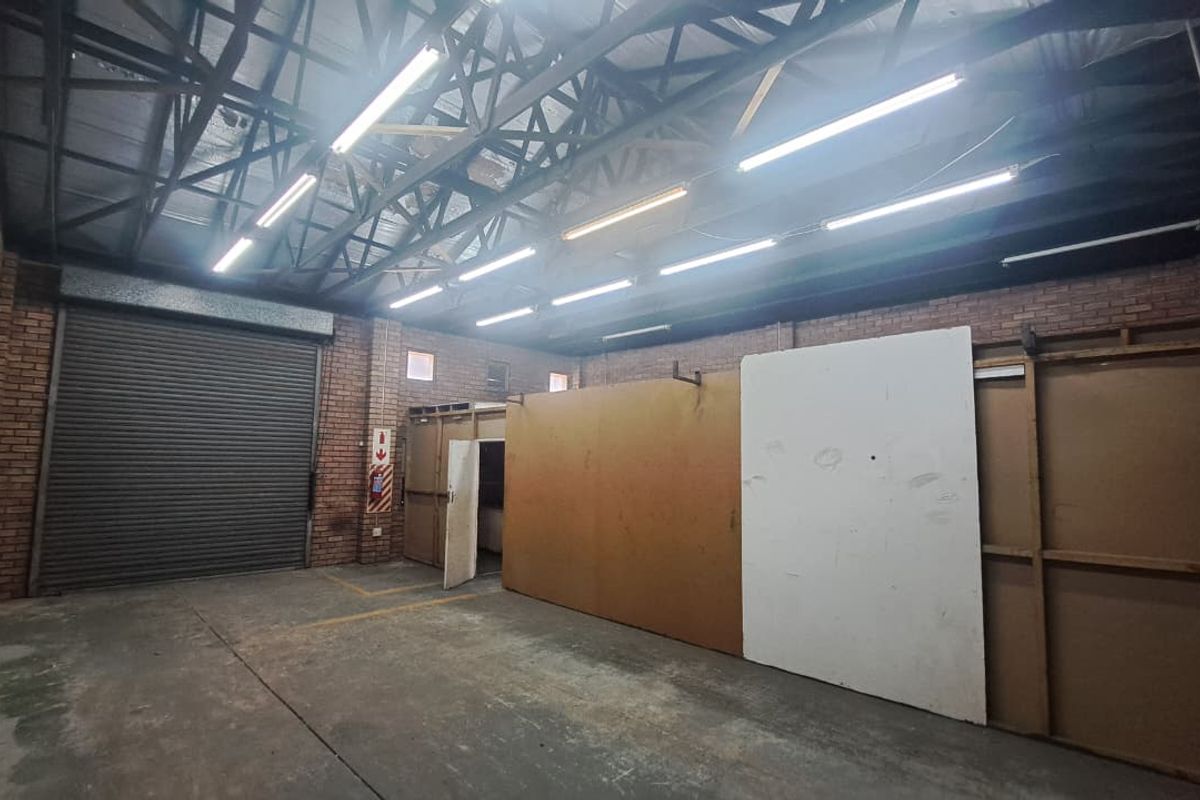 Spacious industrial utility area featuring exposed brick walls, high steel roof trusses, concrete flooring, and a large roller shutter door for easy access.