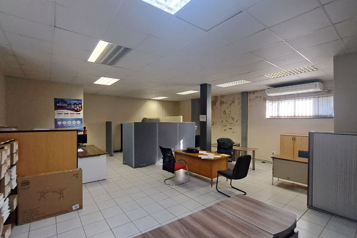 Open-plan office space featuring suspended ceilings, tiled flooring, and a wall-mounted air conditioning unit, currently showing signs of wall surface wear.