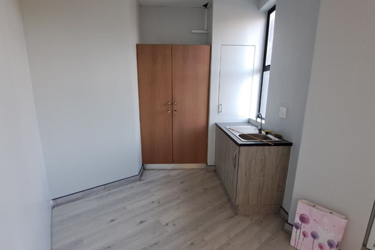 A compact office kitchenette featuring built-in cabinetry, a sink, and light-toned laminate flooring, providing a functional space for staff amenities.
