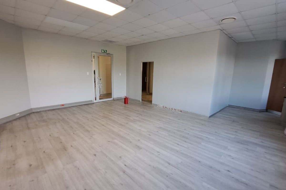 An empty, open-plan office space featuring light wood-look laminate flooring, a suspended ceiling with recessed lighting, and neutral wall finishes.