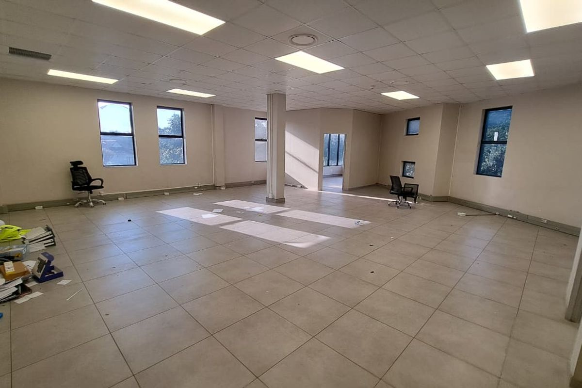 Spacious open-plan office area featuring tiled flooring, suspended ceiling with recessed lighting, and large windows providing natural light.