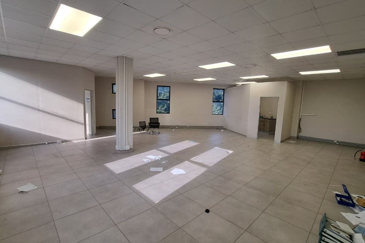 Spacious open-plan office area featuring tiled flooring, a suspended ceiling with recessed lighting, and a central structural column.