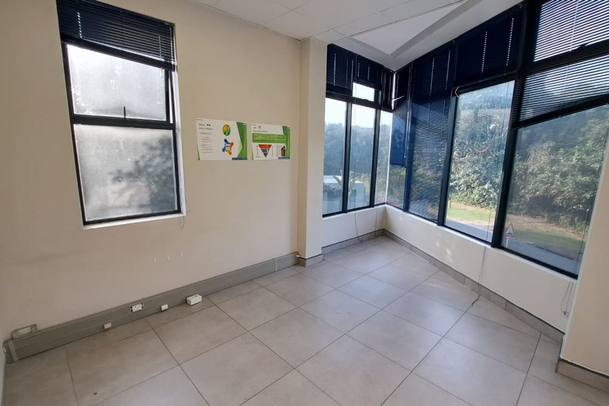A bright, empty office space featuring large windows with venetian blinds, tiled flooring, and a neutral color palette, suitable for a professional workspace.