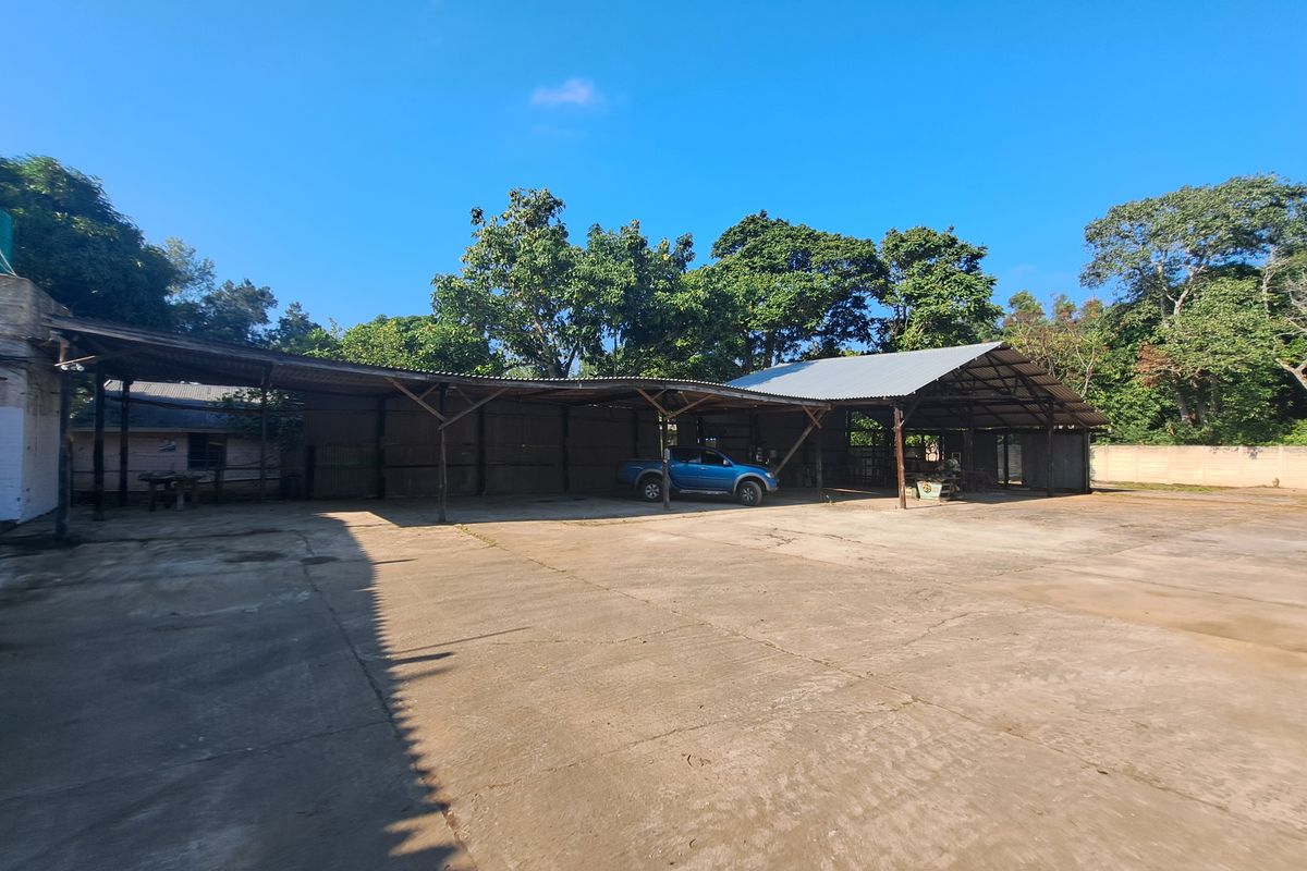Expansive industrial yard featuring a large covered storage area with corrugated metal roofing, concrete flooring, and perimeter boundary walls.