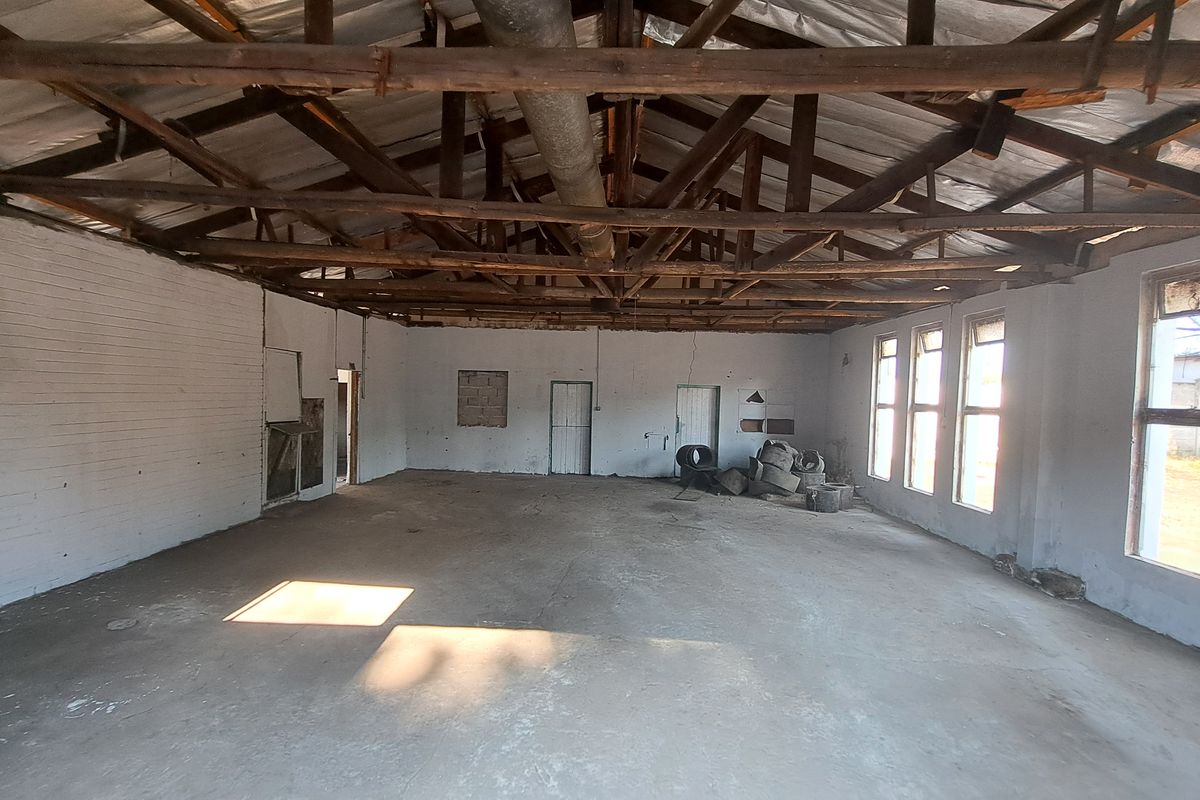Spacious industrial utility area featuring exposed timber roof trusses, concrete flooring, and large windows, offering a blank canvas for renovation or storage use.