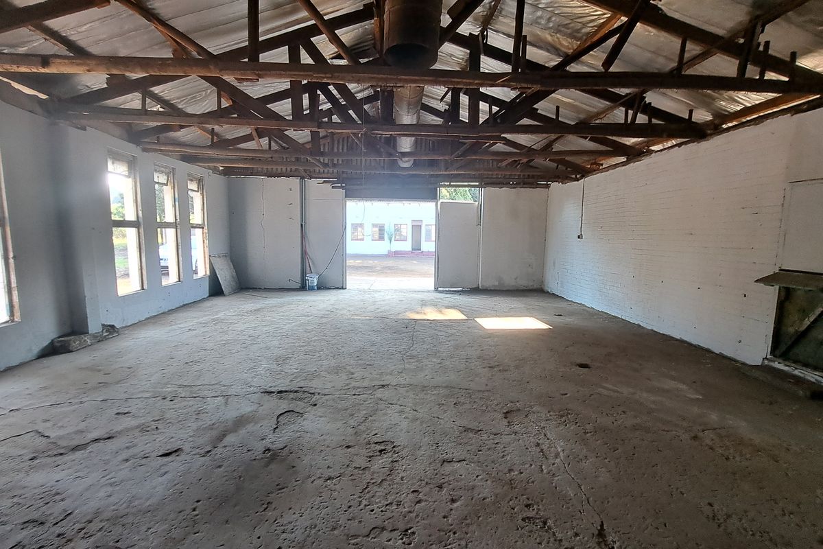 Spacious industrial utility area featuring exposed timber roof trusses, concrete flooring, and large windows, offering a versatile blank canvas for various commercial uses.