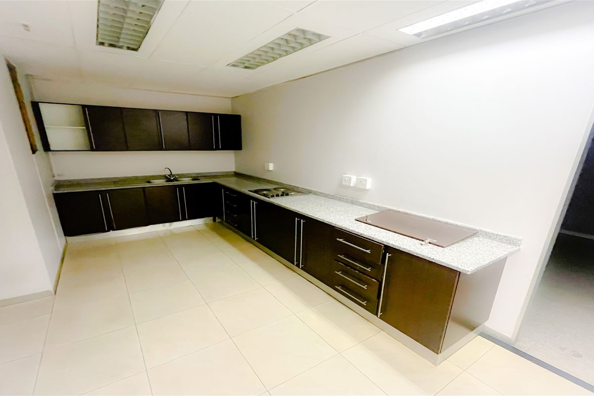 A functional office kitchenette featuring dark cabinetry, granite-style countertops, a stainless steel sink, and recessed ceiling lighting.