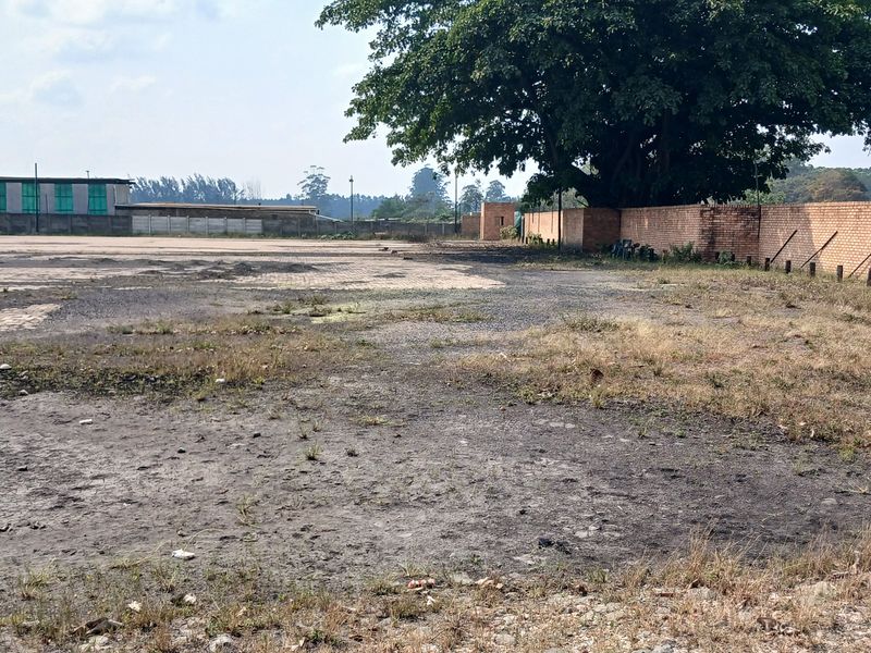 A large, open industrial yard area featuring a brick perimeter wall and a mix of paved and unpaved ground surfaces.