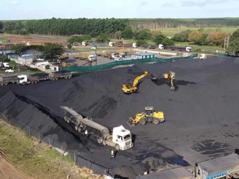 Aerial view of an industrial coal storage and logistics yard featuring heavy machinery and transport trucks.