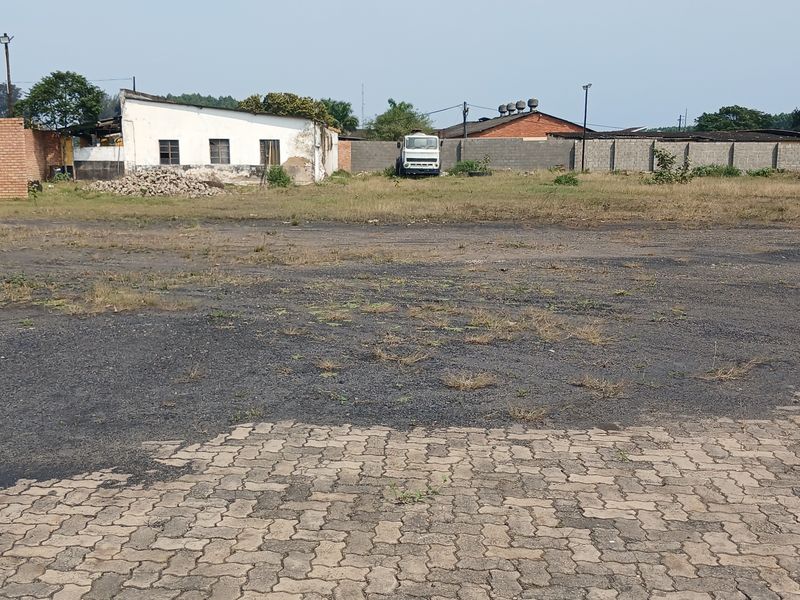 Expansive industrial yard area featuring a paved section, perimeter walling, and an existing industrial building structure in need of maintenance.