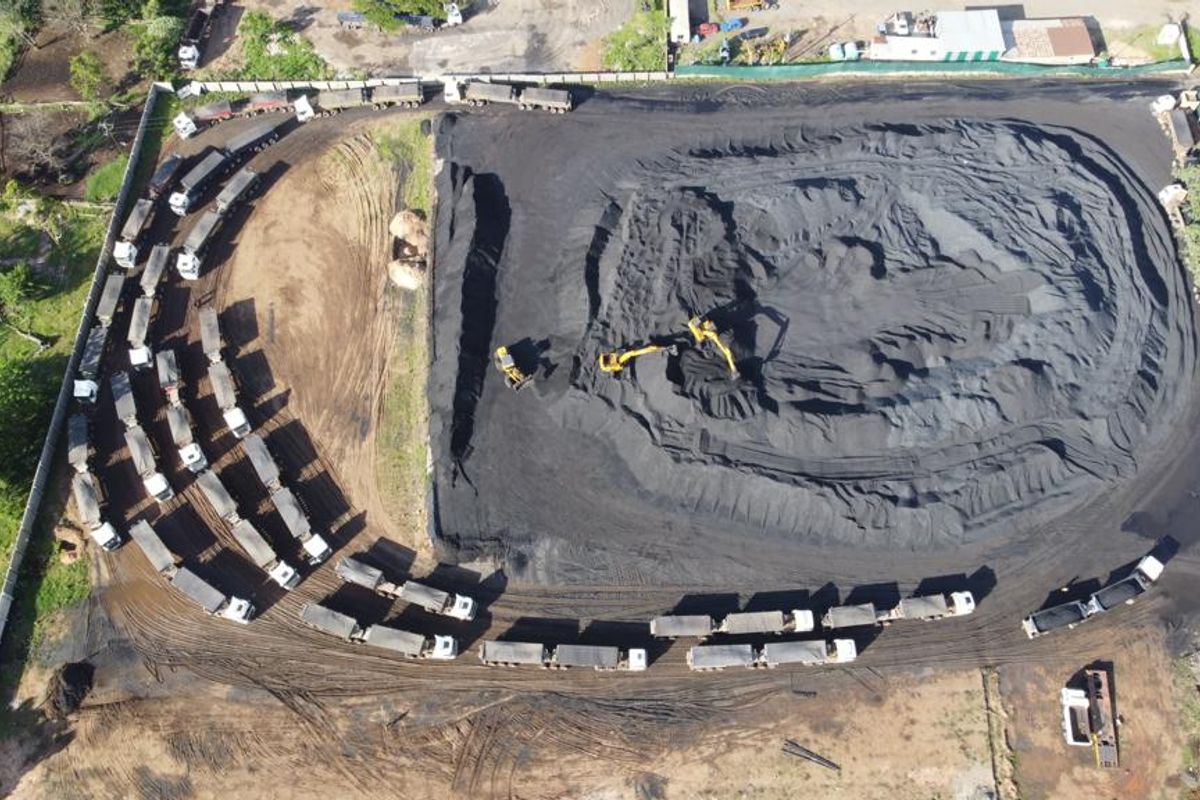 Aerial view of an industrial site featuring a large coal storage yard, perimeter fencing, and heavy vehicle access.