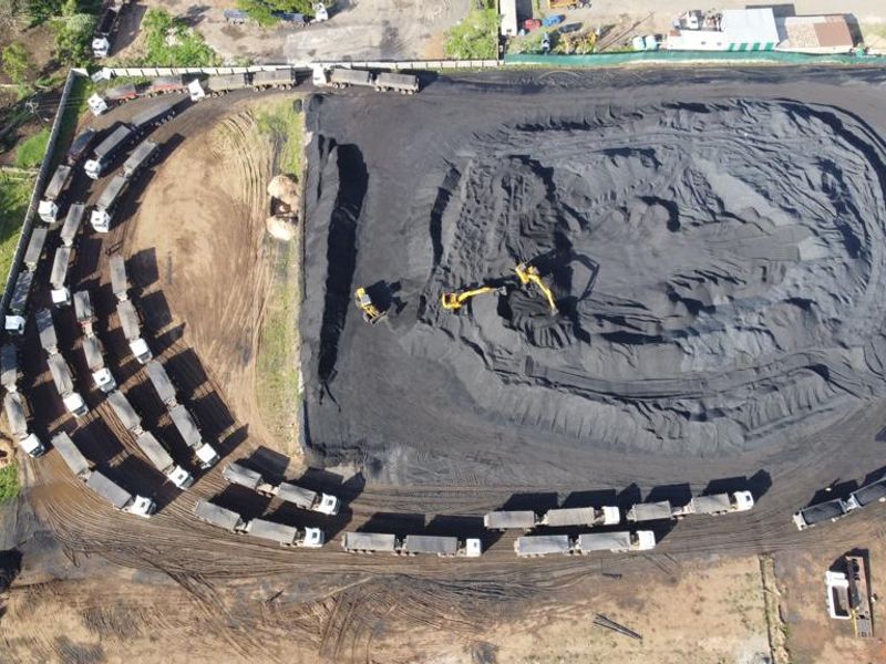 Aerial view of an industrial site featuring a large coal storage yard, perimeter fencing, and heavy vehicle access.