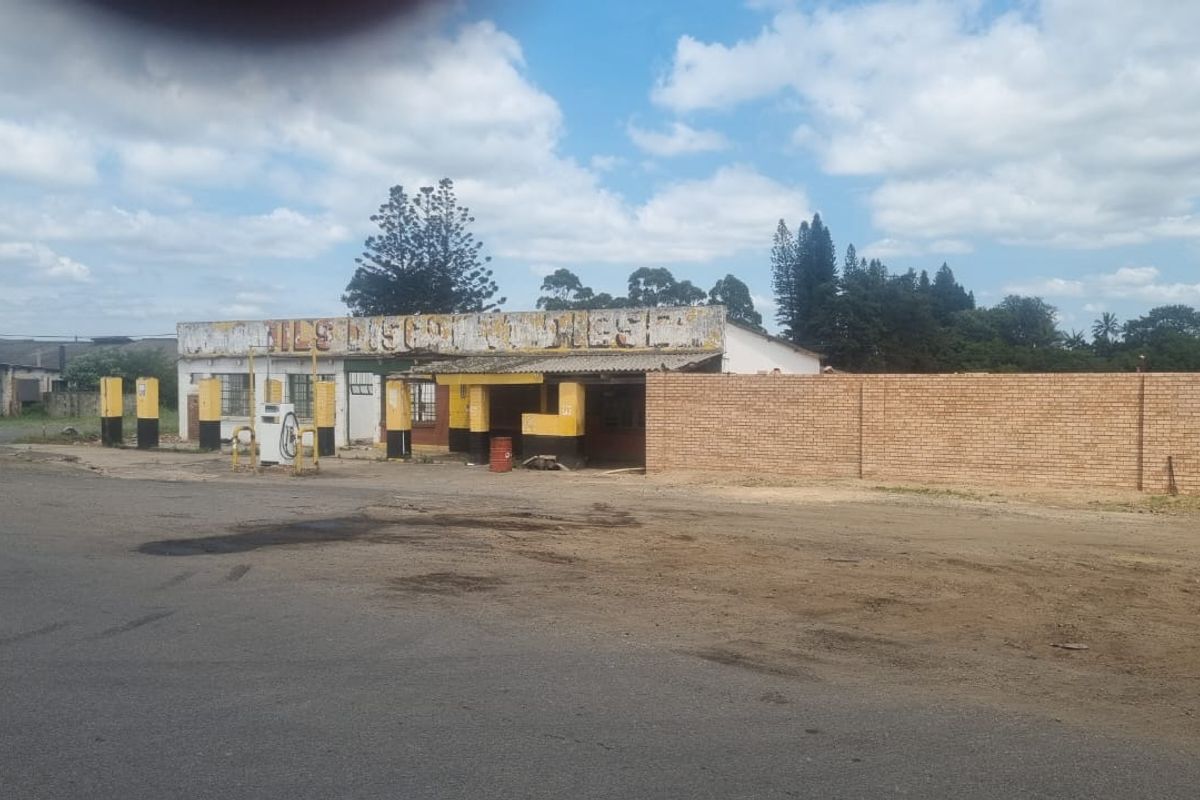 Industrial property featuring a former fuel station forecourt with existing pumps and a brick boundary wall, requiring significant maintenance and refurbishment.