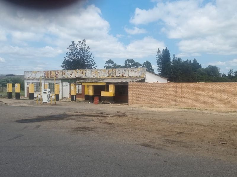 Industrial property featuring a former fuel station forecourt with existing pumps and a brick boundary wall, requiring significant maintenance and refurbishment.