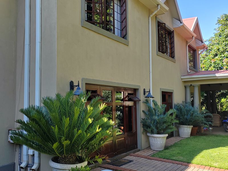 Rear elevation of the lodge featuring timber-framed windows and doors, brick pathways, and a landscaped garden area with a concrete water feature.