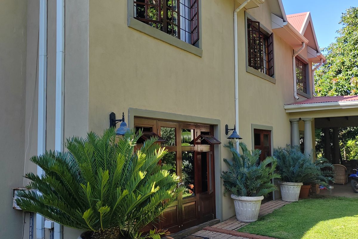 Rear elevation of the lodge featuring timber-framed windows and doors, brick pathways, and a landscaped garden area with a concrete water feature.