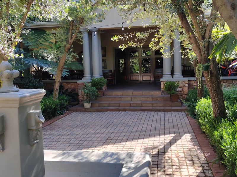 A charming lodge entrance featuring a paved walkway, stone-clad base, classical columns, and a welcoming covered porch with timber-framed glass doors.