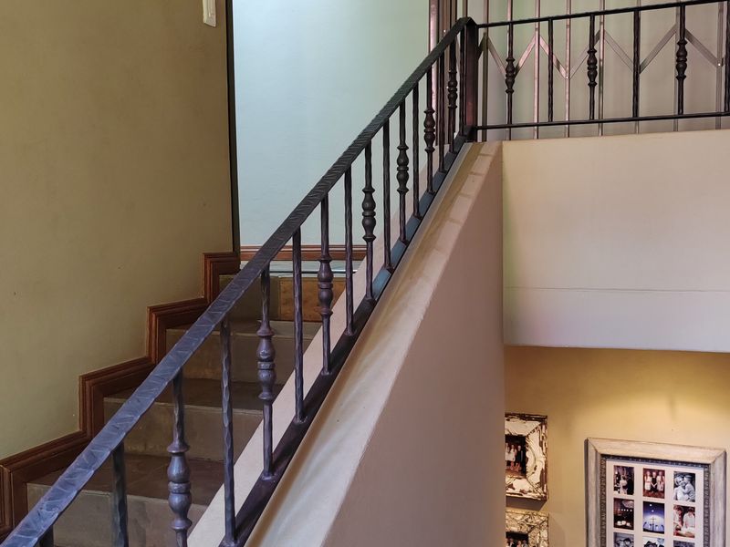 A well-maintained interior hallway featuring a tiled staircase with a decorative wrought iron balustrade and a secure metal gate.