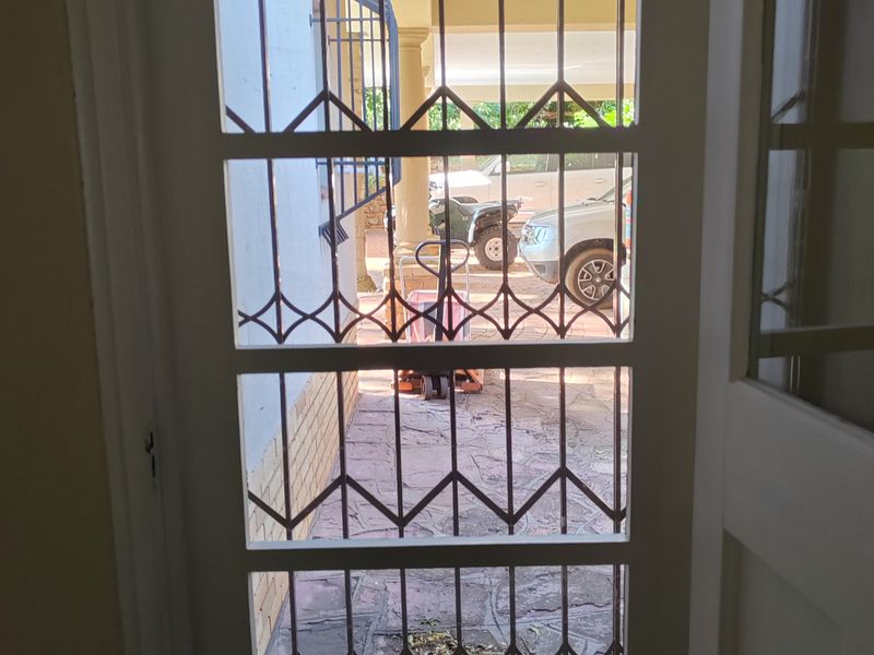 View through a white security gate and glass door looking out onto a paved driveway and covered entrance area.