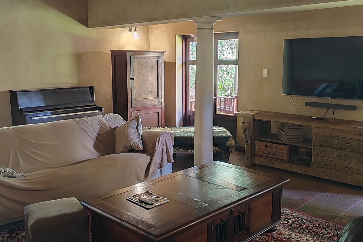 A cozy living room featuring exposed timber ceiling beams, a structural column, and tiled flooring, with direct access to an outdoor area through french doors.