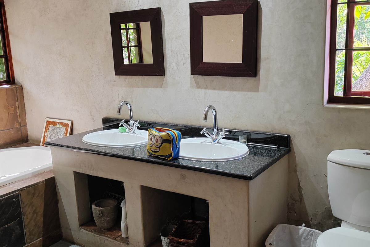 Bathroom featuring a double vanity with granite countertop, drop-in sinks, built-in bathtub, and toilet, with visible wall plaster damage requiring maintenance.