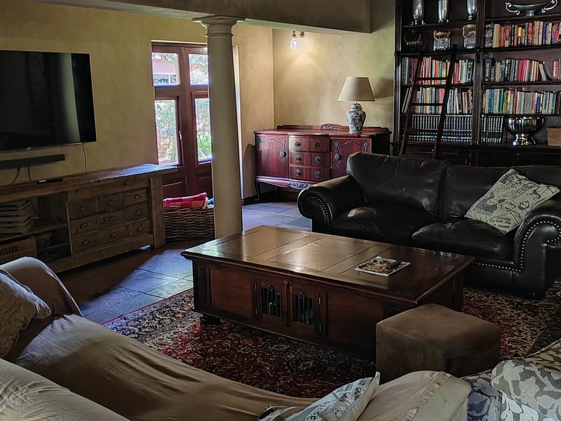 Spacious living room featuring exposed timber ceiling beams, stone tile flooring, and extensive built-in library shelving with a rolling ladder.
