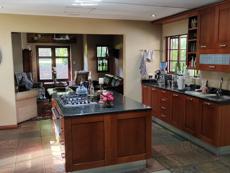 Spacious open-plan kitchen featuring a central island with gas hob, granite countertops, and warm-toned cabinetry, seamlessly flowing into the adjacent living area.