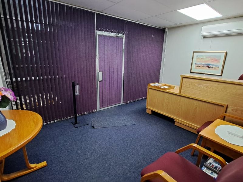 A functional office reception area featuring a built-in wooden desk, suspended ceiling, and split-system air conditioning unit.