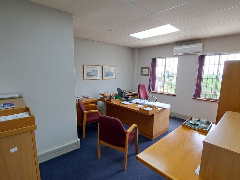 A functional office space featuring carpeted flooring, grid windows, and a wall-mounted air conditioning unit, providing a professional environment for work.