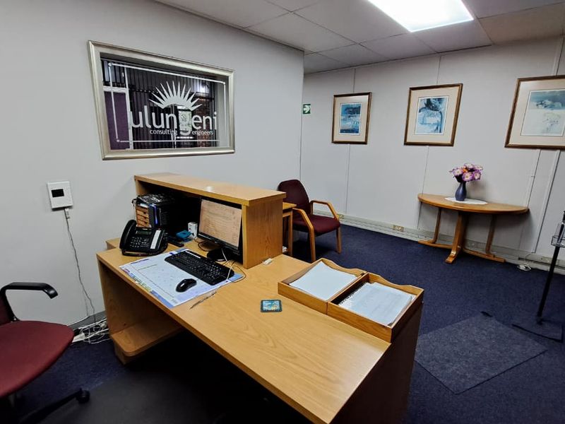 A functional office space featuring a suspended ceiling, recessed lighting, and carpeted flooring, suitable for a professional work environment.
