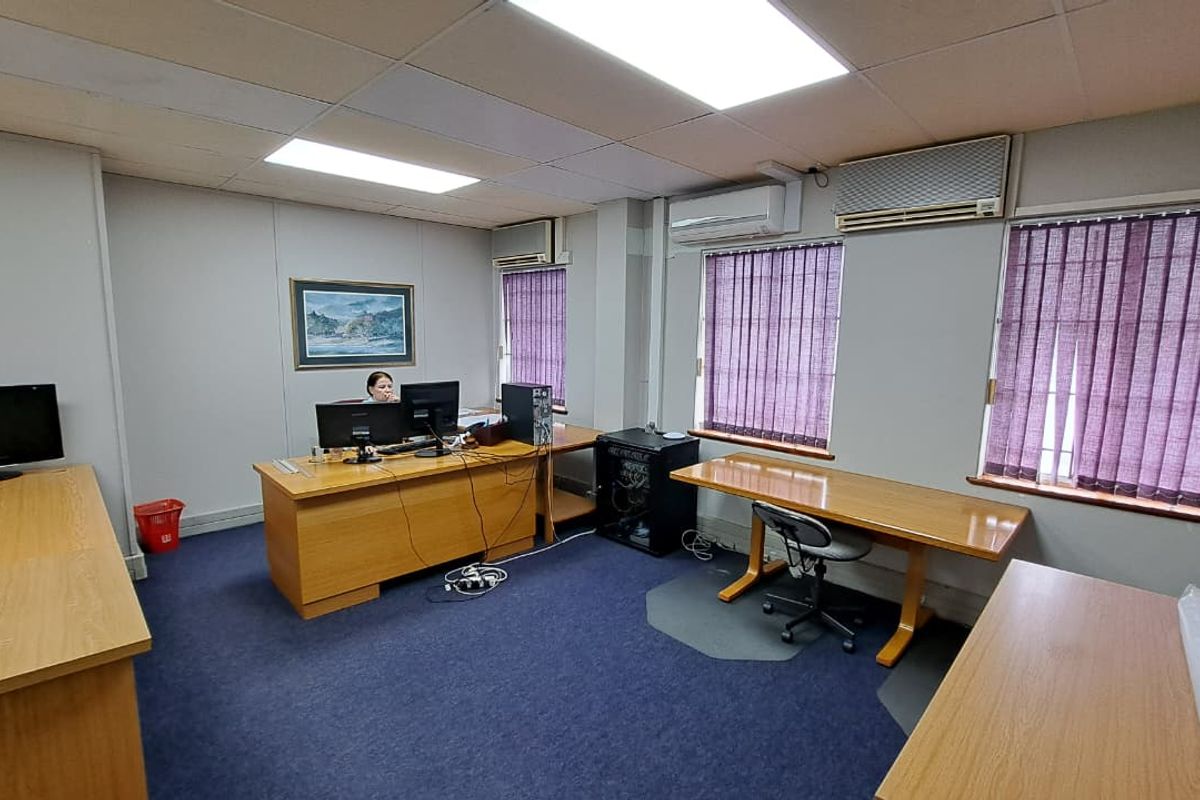 A functional office space featuring suspended ceilings, recessed lighting, split-system air conditioning units, and vertical blinds on the windows.