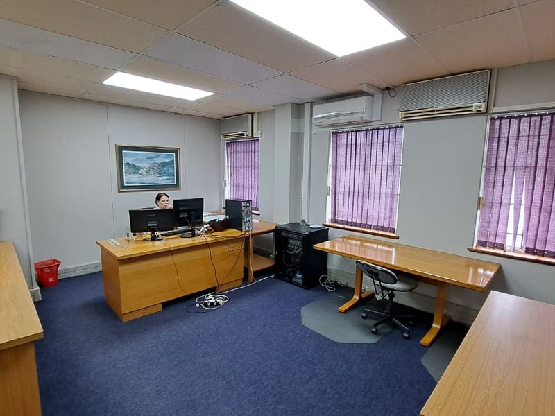 A functional office space featuring suspended ceilings, recessed lighting, split-system air conditioning units, and vertical blinds on the windows.