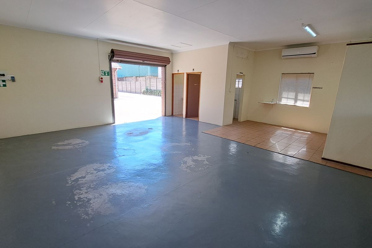Spacious open-plan office area featuring a roller shutter door, air conditioning, and a mix of painted concrete and tiled flooring.