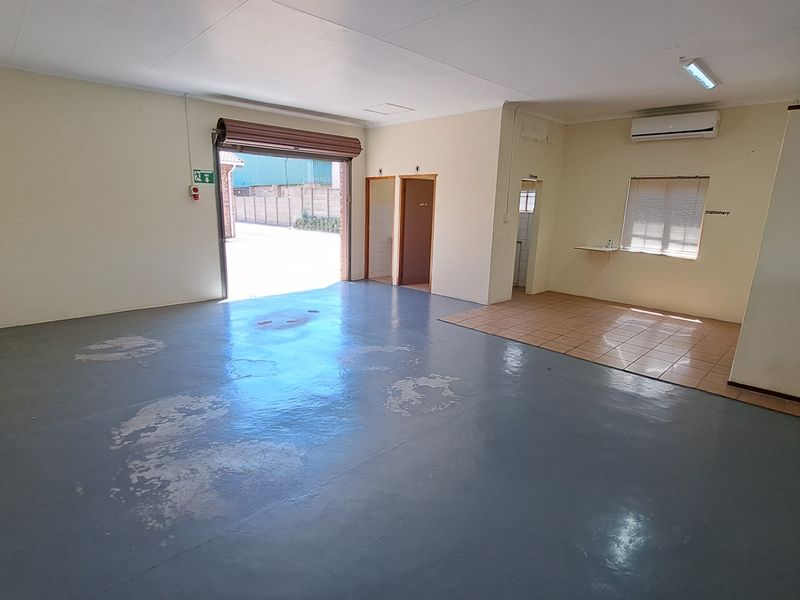 Spacious open-plan office area featuring a roller shutter door, air conditioning, and a mix of painted concrete and tiled flooring.