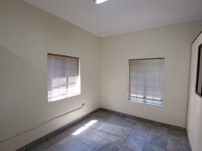 A clean, empty office space featuring tiled flooring, neutral walls, and dual windows with fitted venetian blinds.