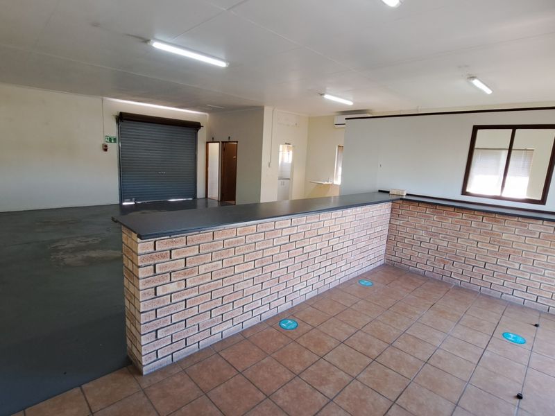 Open-plan office space featuring a brick service counter, tiled flooring, and a secure roller shutter door, suitable for various commercial or administrative uses.
