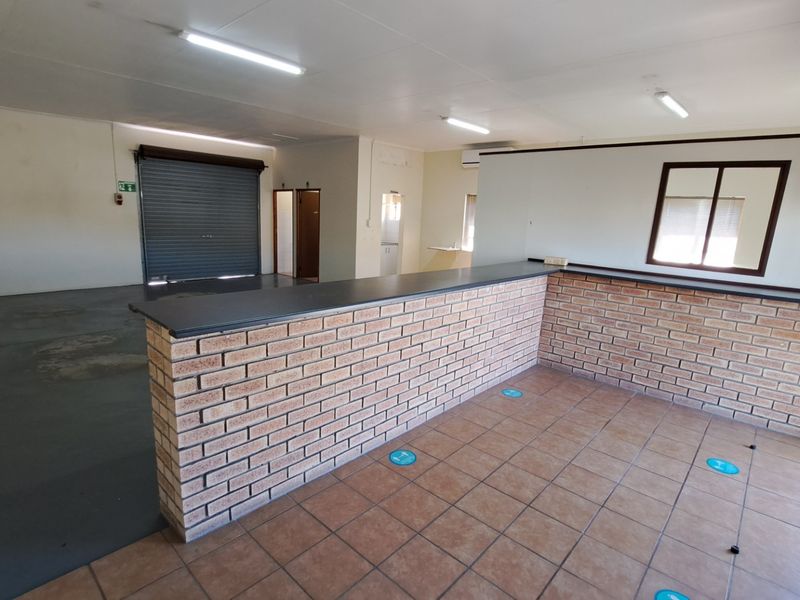 Open-plan office space featuring a brick service counter, tiled flooring, roller shutter door access, and integrated fluorescent lighting.