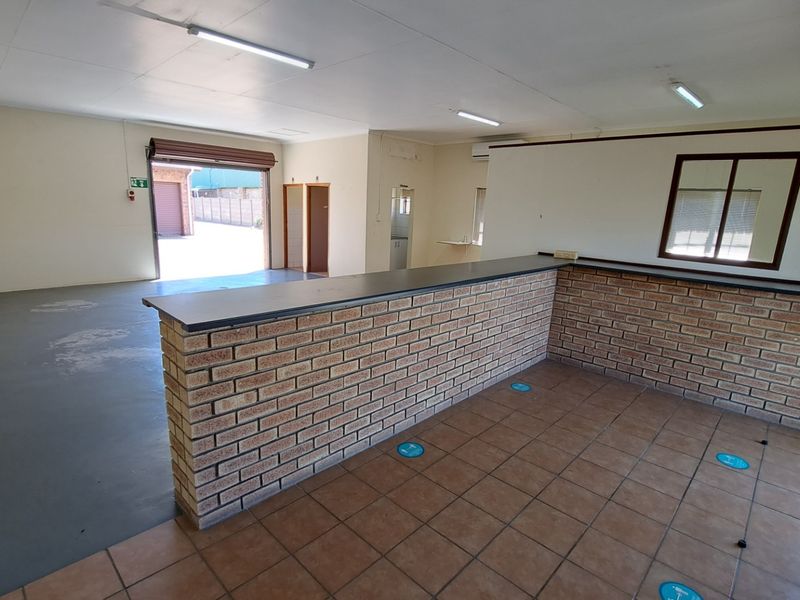 Open plan office space featuring a brick reception counter, tiled and epoxy flooring, and direct access via a roller shutter door.