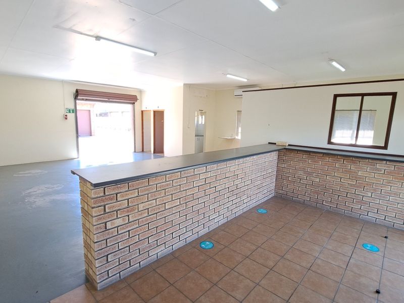 Open plan office space featuring a brick service counter, tiled flooring, fluorescent lighting, and a roller shutter door for easy access.