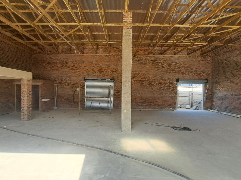 Spacious industrial utility area featuring exposed brick walls, timber roof trusses, concrete flooring, and roller shutter access, suitable for workshop or storage use.