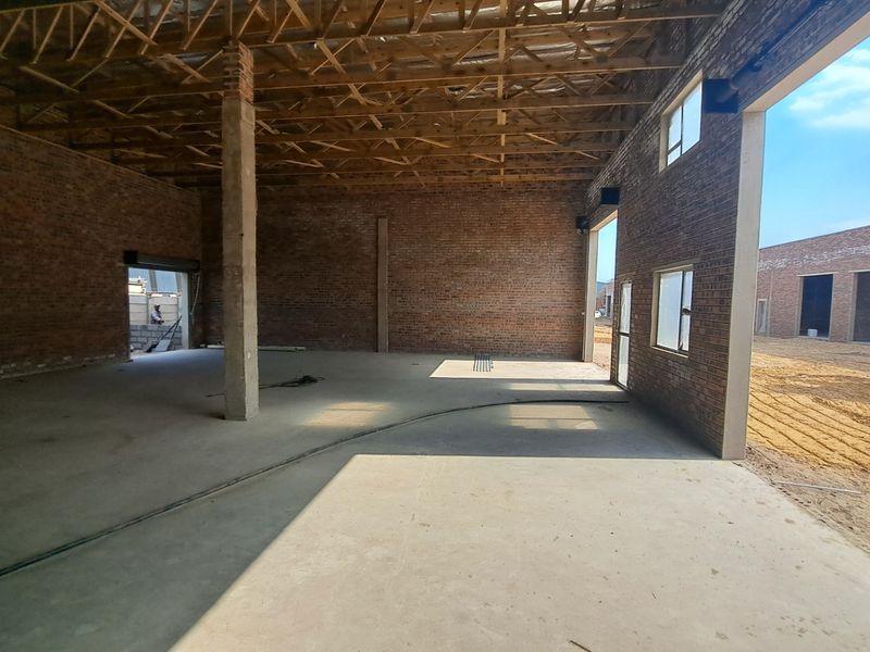 Spacious industrial utility area featuring exposed brick walls, concrete flooring, and open timber roof trusses, currently in an unfinished construction state.