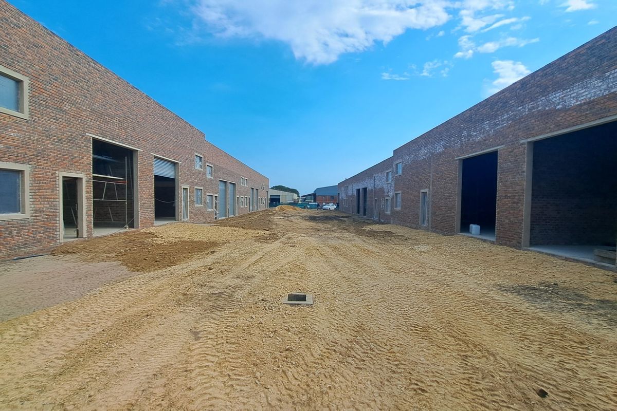 View of an industrial development site featuring face brick warehouse units with roller shutter doors and unfinished ground works.