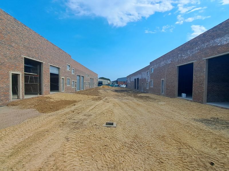 View of an industrial development site featuring face brick warehouse units with roller shutter doors and unfinished ground works.