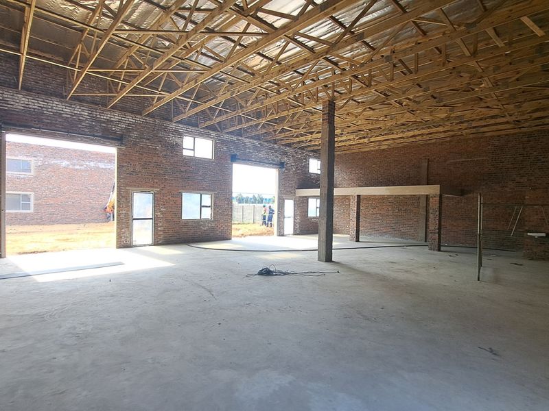 Spacious industrial warehouse unit featuring exposed brick walls, high timber truss ceilings, concrete flooring, and a mezzanine level, currently in an unfinished state.