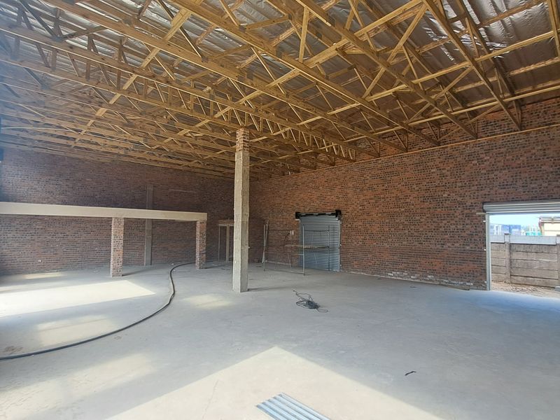 Spacious industrial warehouse unit featuring exposed brick walls, high timber roof trusses, concrete flooring, and multiple roller shutter access points.