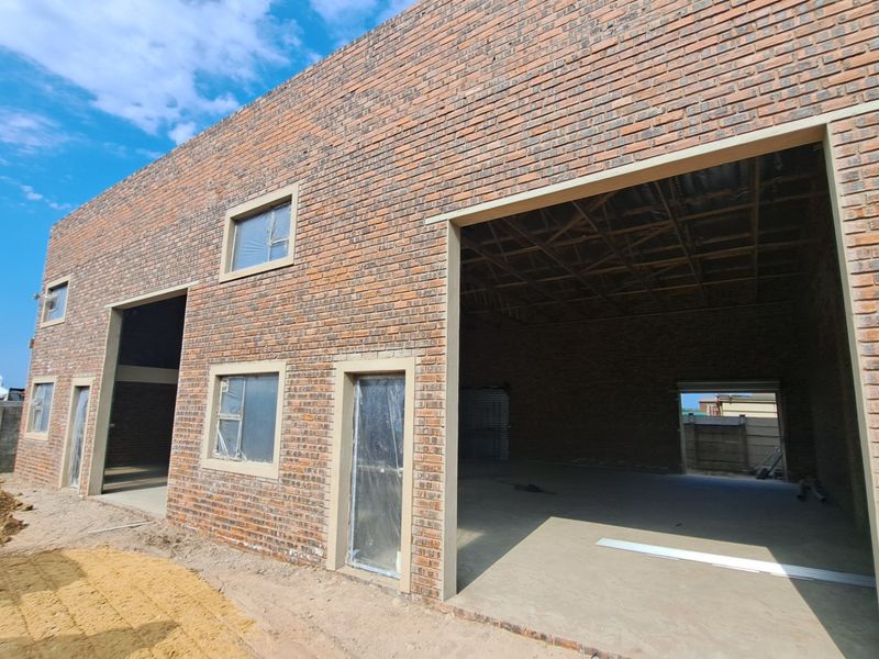 Exterior view of an industrial warehouse under construction, featuring face brick facade, large roller door openings, and exposed timber roof trusses.