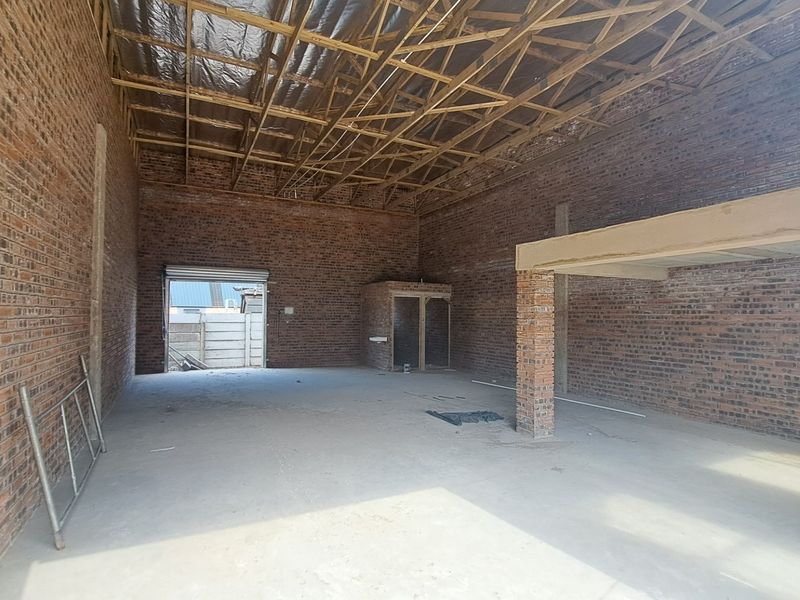 Spacious industrial warehouse unit featuring exposed brick walls, high timber roof trusses, concrete flooring, and a mezzanine level, suitable for various commercial or storage uses.